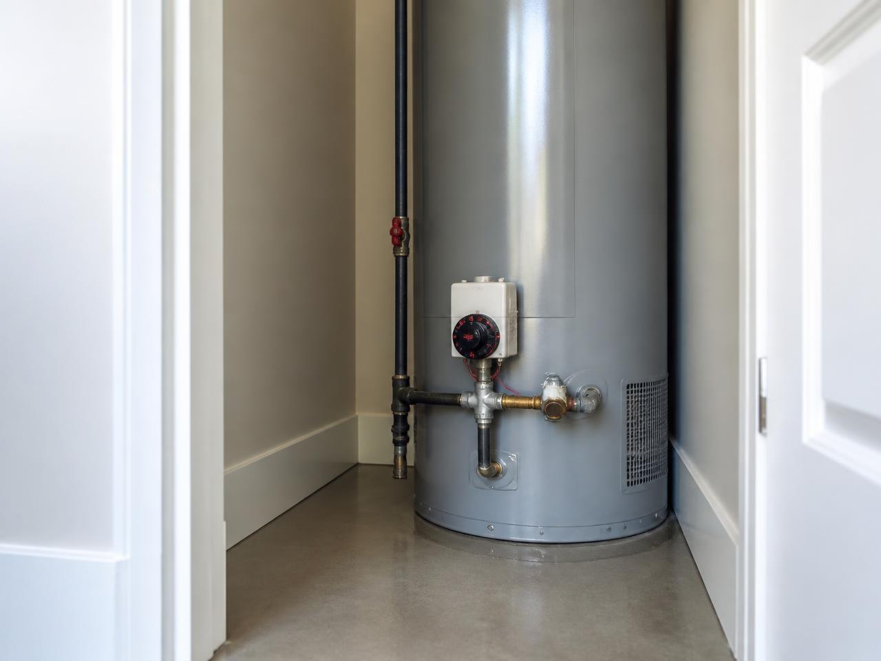 Residential tank-style water heater in a utility closet with a small amount of water collecting at the base